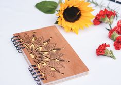 a wooden notebook sitting on top of a table next to red flowers and a sunflower