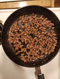 a frying pan filled with ground beef on top of a stovetop next to a burner