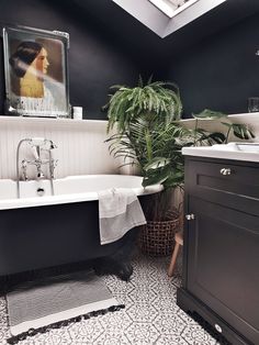 a black and white bathroom with a claw foot tub, potted plant and sink