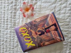 a book sitting on top of a white bed next to a pink and orange flower