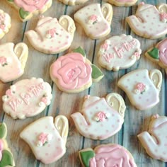 decorated cookies with pink and white frosting on a wooden table next to teapots