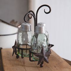 two glass jars are sitting on a table with a metal holder holding starfishs