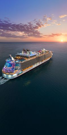 a large cruise ship in the middle of the ocean at sunset, with its lights on