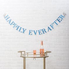 a happy ever after banner hanging on a white brick wall next to a table with drinks