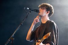 a young man singing into a microphone while holding a guitar in front of his face