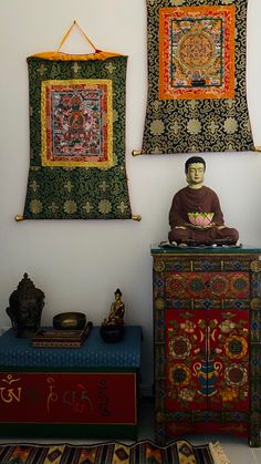 a buddha statue sitting on top of a wooden cabinet next to two wall hangings