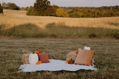 two hay bales with pumpkins and pillows on a blanket in the middle of a field