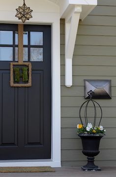 a black front door with a cross hanging on it's side and flowers in the planter