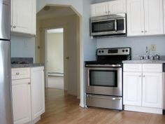 an empty kitchen with stainless steel appliances and white cabinets