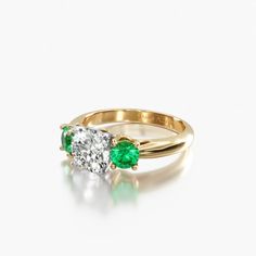 an emerald and diamond engagement ring on a white background, with the top half in yellow gold