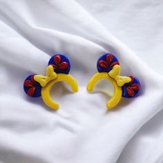 two yellow and blue ear clips with red bows on them sitting on a white cloth