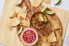 a bowl of mexican macaroni dip next to tortilla chips and lime wedges