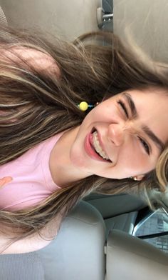 a woman smiling and sitting in the back seat of a car with her hair blowing in the wind