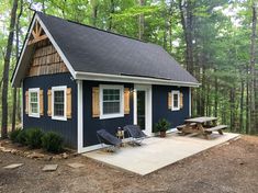 a small blue cabin in the woods with picnic table and chairs on the front porch