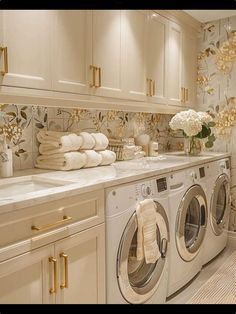 a washer and dryer in a room with white cabinets, gold handles and flowers on the wall