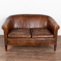 a brown leather couch sitting on top of a wooden floor next to a white wall