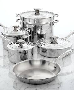 a set of pots and pans on a marble counter top with the lids off