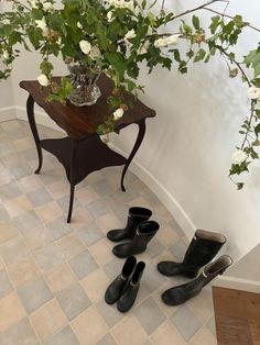 there are four pairs of black shoes on the floor next to a vase with white flowers