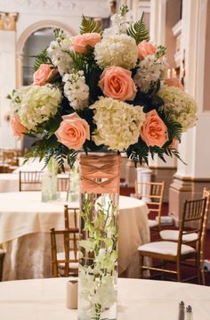 a vase filled with white and pink flowers on top of a table next to chairs