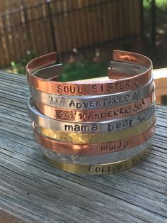 four different bracelets with words on them sitting on a wooden table outside in front of a fence