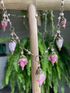 a wooden pole with some pink glass beads hanging from it's sides and a potted plant in the background