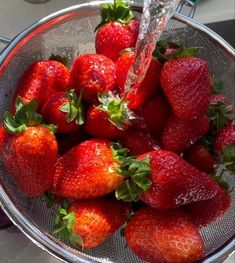 fresh strawberries are being washed in a colander