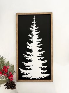 a white christmas tree on a black background in a wooden frame next to red berries and pine cones