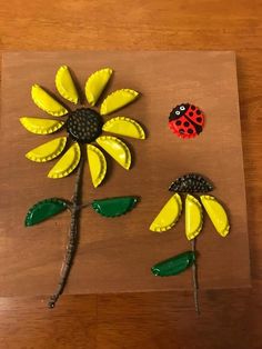 two plastic flowers and a ladybug sitting on top of a wooden table next to each other