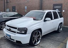 a white suv parked in front of a brick building next to two other black cars