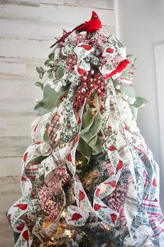 a christmas tree decorated with red and white ribbons, holly wreaths, and birds