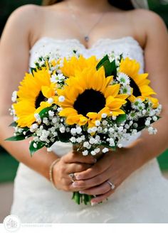 a bride holding a bouquet of sunflowers and baby's breath