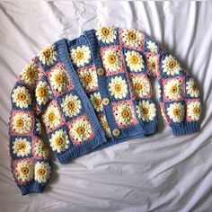 a crocheted sweater with flowers on it laying on a white bed sheet,