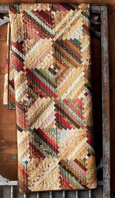 a multicolored quilt hanging on the side of a wooden wall next to an old window