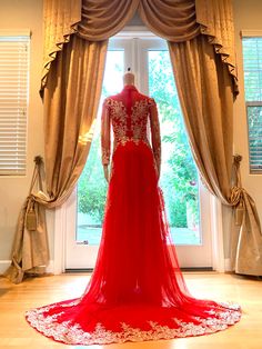 a mannequin dressed in a red gown stands next to a window with curtains