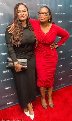 two women standing next to each other in front of a red carpet and blue wall