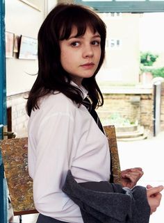 a woman in a white shirt and black tie holding a piece of clothing while standing next to an open door