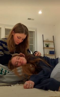 two young women laying on the floor while one woman combs her hair and another watches