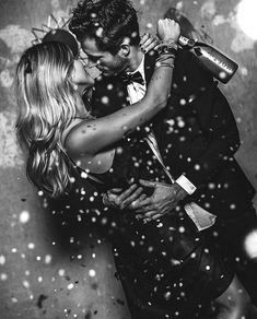 a man and woman are kissing in front of snow falling down on the ground with their arms around each other