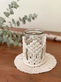 a crocheted candle holder sits on a wooden table next to a potted plant