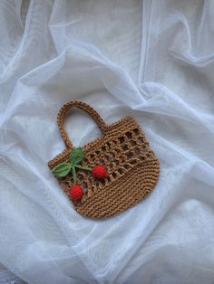 a crocheted strawberries purse is laying on a white cloth covered bed sheet