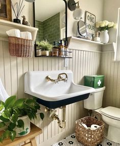 a white sink sitting next to a toilet in a bathroom under a mirror and potted plant