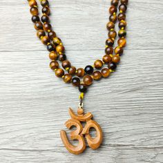 37" Unique Handcrafted Top Quality Tiger Eye Regal Beaded Knotted Necklace with Sandalwood Om Carved Scared Symbol. Sacred Amulet, Protection and Blessing Jewelry Gift. Handcrafted, Comes with A Velvet Pouch. ✥ Mala Necklace: 37" Long - 8mm beads ❀❀❀ Please look closely at photos as part of item description, the product in the images is as the one you will receive and is sold "as is". Please review the description and images prior to purchasing to ensure this item meets your satisfaction. We wel Brown Beaded Necklaces For Meditation And Festivals, Brown Beaded Holistic Mala, Holistic Brown Beaded Mala, Brown 8mm Beads Mala For Festival, Brown Beaded Mala For Festivals, Brown Mala With 8mm Beads For Festival, Brown Wooden Beads For Festivals, Festival Brown Beaded Mala, Bohemian Brown Mala For Festivals