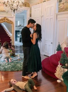 a man and woman kissing in the middle of a living room with christmas decorations on the floor