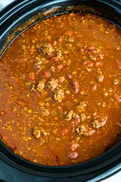 a slow cooker filled with chili and meatballs on top of a white table