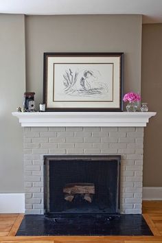 a white brick fireplace with some pink flowers on the mantel and framed artwork above it