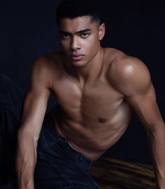 a shirtless young man sitting on the floor posing for a photo in front of a dark background