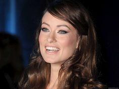 a woman with long brown hair and blue eyes smiles at the camera while wearing a black dress