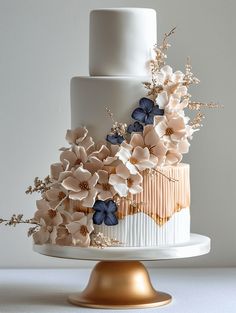 a white and gold wedding cake with flowers on top