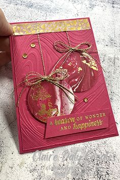 a hand holding a red card with gold foil and a heart shaped ornament