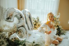 a woman sitting on top of a bed in front of an air filled number balloon